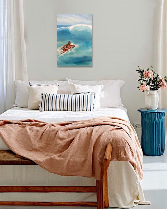 Bedroom with a painting of a surfer on the wall, a vase with flowers on a side table, and a pink blanket on the bed.