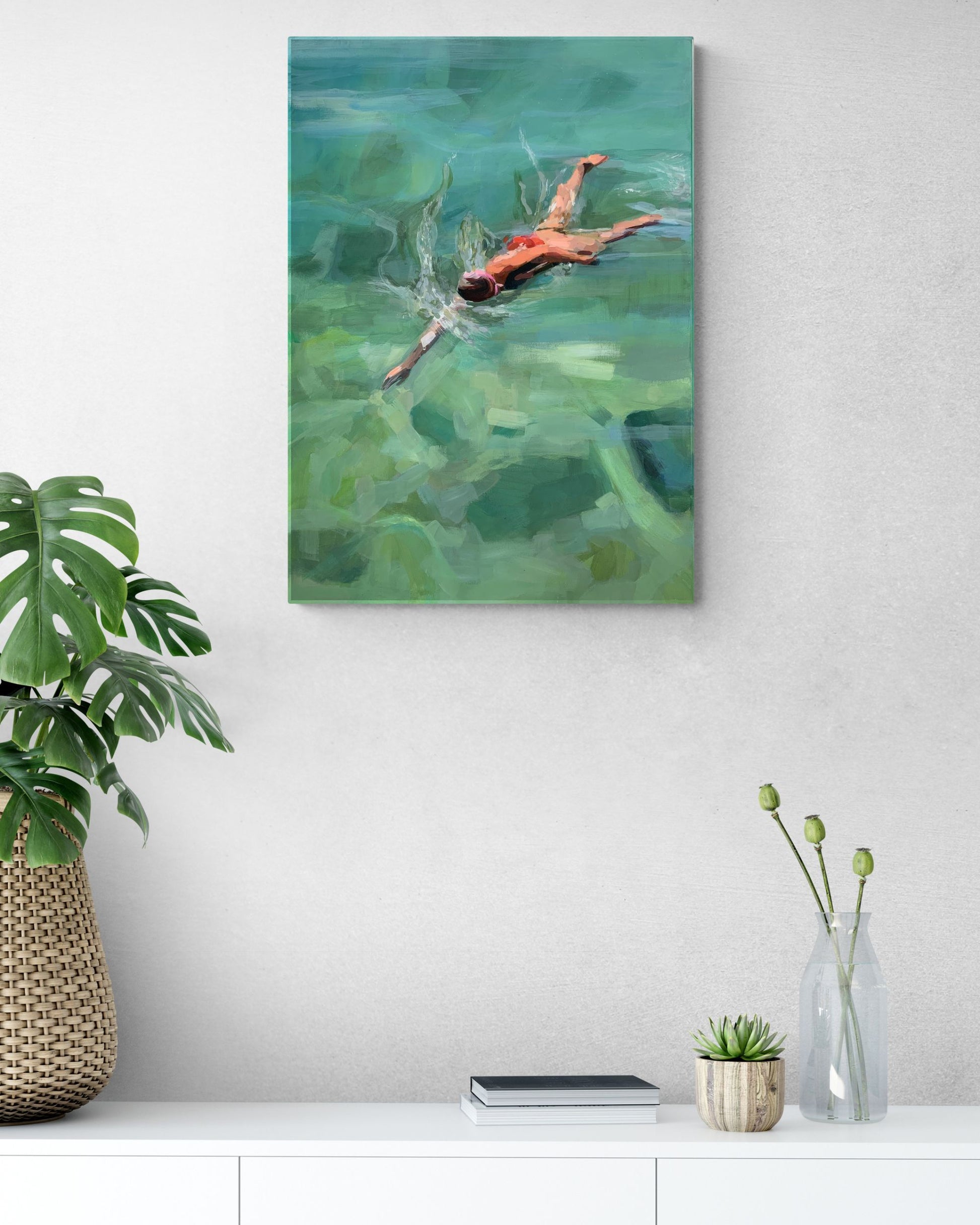 Original painting of a swimmer in green water on a white wall above a shelf with decorative items.